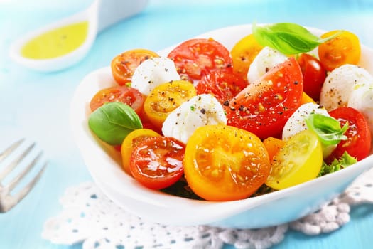 Close-up of a bowl of fresh and healthy Mediterranean salad with mozzarella cheese, tomatoes and basil leaves with a spoon of olive oil in the background