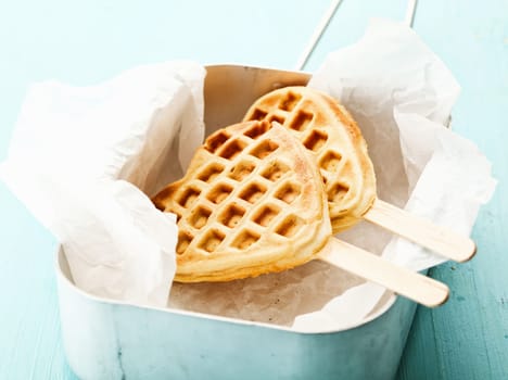 Fun crisp golden heart-shaped waffle popsicle with the traditional honeycomb pattern and a wooden stick on crumpled paper in a tin