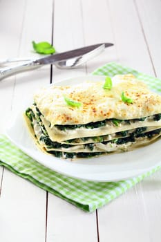 Serving of fresh baked vegetarian spinach lasagna on a plate over a napkin and an old white wooden table