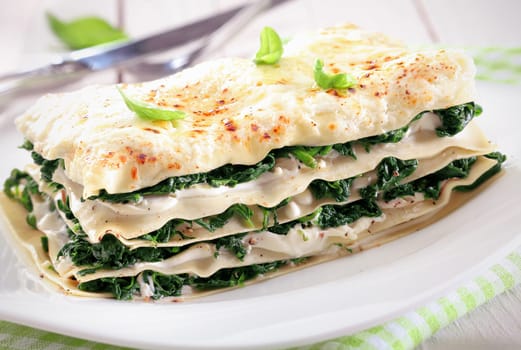 Close-up of a fresh baked vegetarian spinach lasagna on a plate over a napkin and an old white wooden table