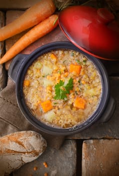 Top view of a warm and delicious freshly made pot of soup with raw carrots, chickpeas and a loaf of rustic bread