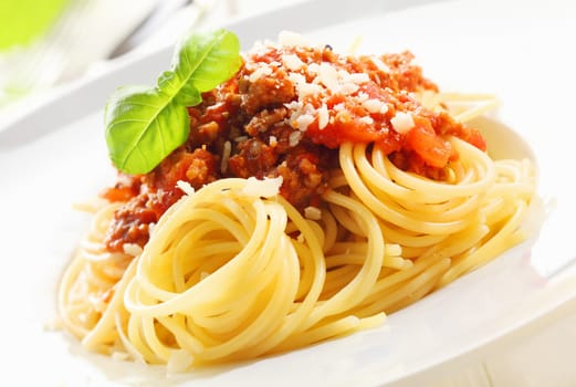 Closeup of coiled cooked Italian spaghetti topped with Bolognese sauce and garnished with fresh basil leaves