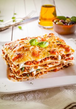 Portion of traditional durum wheat lasagne with bolognaise sauce, beef mince and cheese in alternating layers on a white plate