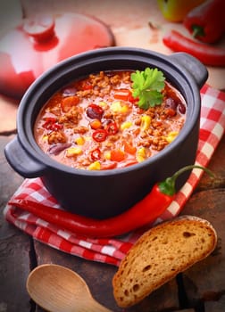 Hot and spicy fresh made Mexican chili still in an iron pot, with a raw chili-pepper and a slice of bread
