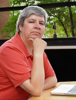 middle-aged woman seated at table with laptop, looking at you