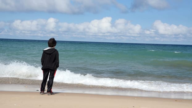 Boy watching waves wash ashore in Lake Michigan beach