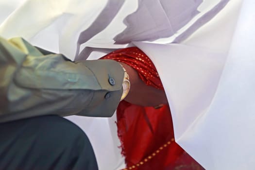 Horizontal color capture taken at a hindu wedding in Surat India. Part of the ceremony is that the couple hold hands covered by a silk sheet whilst the rituals are being performed by clergy