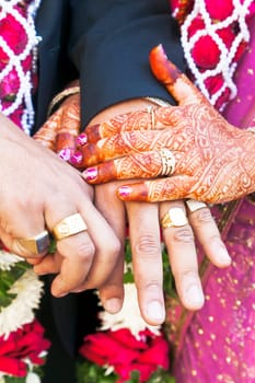 Vertical color portrait taken at a hindu wedding in Surat India. Photo session after the ceremony of the happy hand holding couple displaying their rings of matrimony and the brid lays her claim