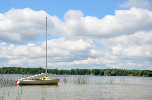 Sailboat moored at a quiet lake, with partly cloudy skies