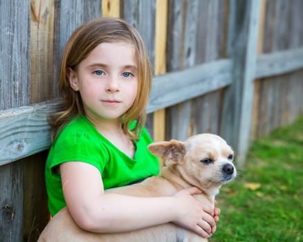 Blond happy girl with her chihuahua doggy portrait on backyard fence