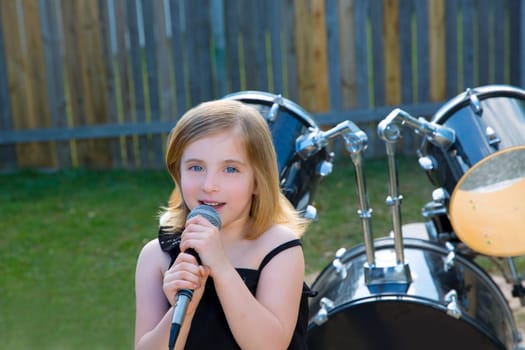 Blond kid girl singing in tha backyard with drums behind