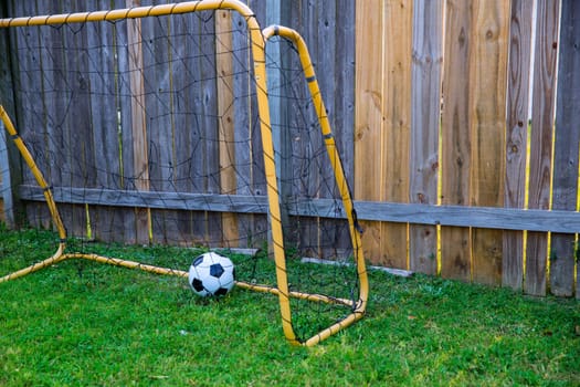 Backyard chldren soccer goal at the wood fence with leather ball on grass