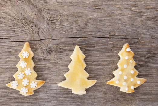 three different decorated christmas tree cookies on a wooden background with copy space