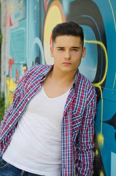 Handsome young man against colorful graffiti covered wall
