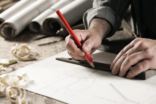 Closeup  view of a carpenter using a red pencil to draw a line on a blueprint