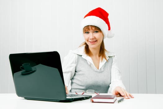 Smiling girl in a Christmas hat with a laptop at the office
