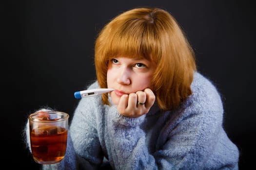 sick girl with tea and a thermometer on a black background