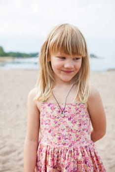 Smiling young barefoot girl wearing pink patterned dress at beach looking to side