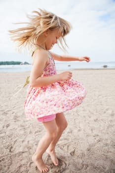 Young barefoot girl with pink patterned dress having fun at beach with ocean in background