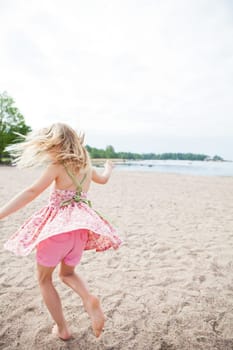 Young barefoot girl with pink patterned dress and pants having fun at beach with ocean in background