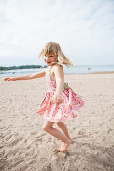 Smiling young barefoot girl with pink patterned dress having fun at beach with ocean in background
