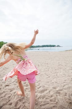 Young barefoot girl with pink patterned dress and pants having fun at beach with ocean in background