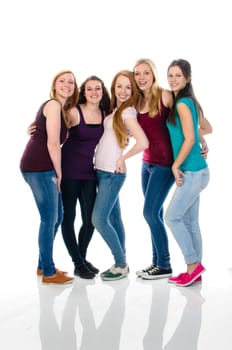 A group of five young teenager girls in casual wear stand together and making happy faces to the camera, isolated again white background.