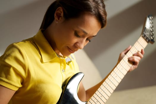 beautiful mid adult woman playing electric guitar at home, sitting on sofa