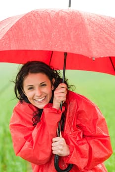 Wet young girl in raincoat enjoying rainfall with umbrella