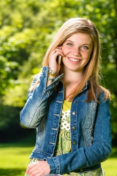 Lively young girl talking on her phone outside during spring