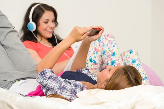 Teen girls relaxing on bed with mobile phone and headphones