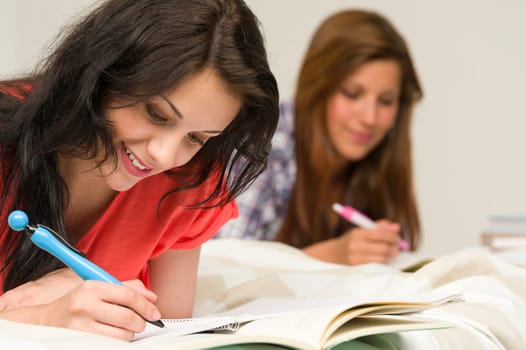Young teenage girls lying and studying on bed