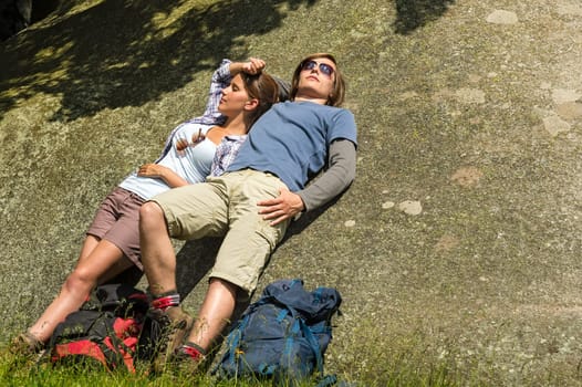 Resting Caucasian couple enjoying sunshine on rock backpack