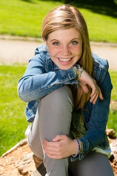 Cheerful teenage girl sitting in the park looking at camera