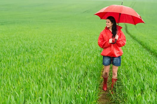 Smiling young woman standing on meadow on rainy day
