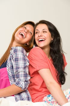 Playful sisters sitting back-to-back and laughing