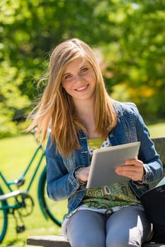 Teenage girl sitting with digital tablet in the sunny park