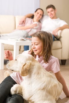 Playful girl petting family dog with parents sitting on couch