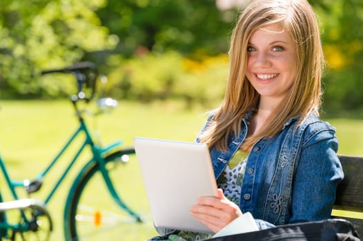 Adolescent girl using tablet computer in the park summertime