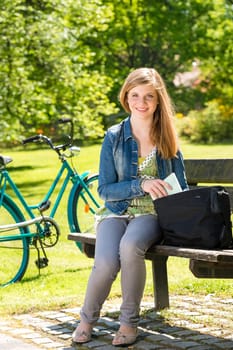 Teenager student girl sitting on bench bicycle in the background