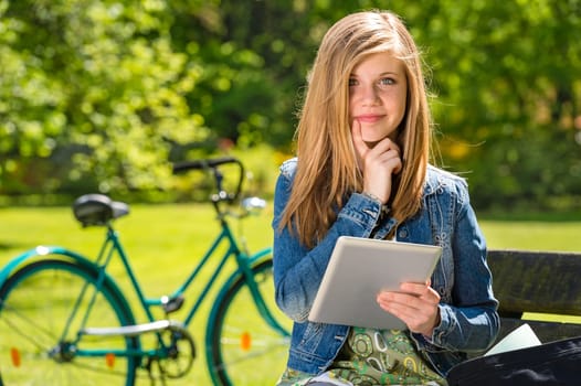 Pensive teenager outside in the park with digital tablet