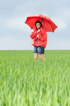 Elated teenage girl holding red umbrella on meadow