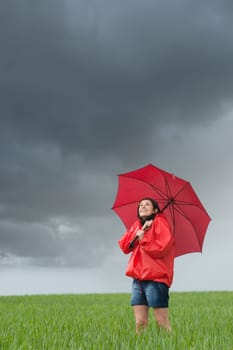 Lively girl daydreaming on rainy day on field with umbrella