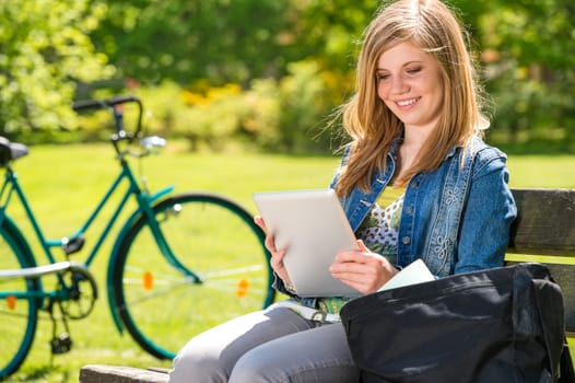 Young girl reading on tablet sitting in the park
