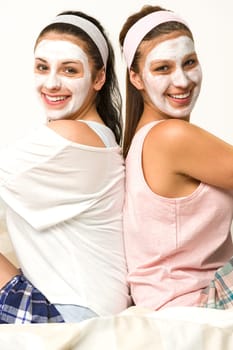 Two female friends sitting back-to-back with white facial mask