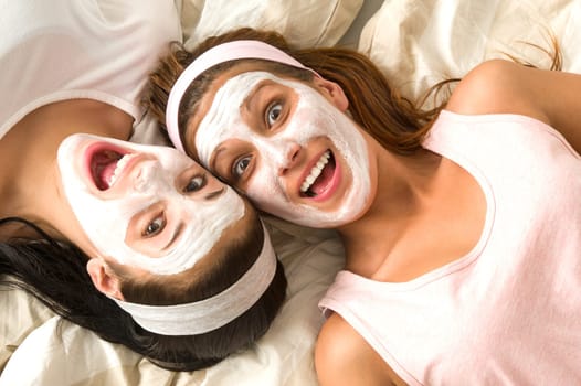 Serene girls lying on bed wearing cosmetic mask and laughing