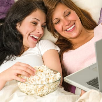 Pretty sisters lying on bed watching funny movie