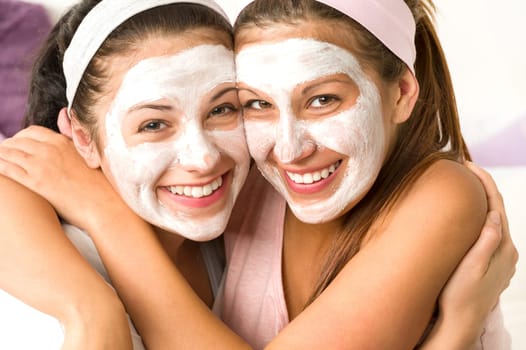 Blissful girls applying white facial mask hugging each other