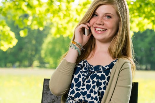 Smiling young girl using her mobile phone outside springtime