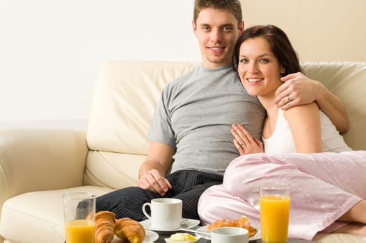 Cheerful couple sitting on couch looking at camera